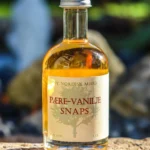 Flaske med Pære-Vanilje Snaps på 5 cl med gylden væske, placeret på en sten udendørs.