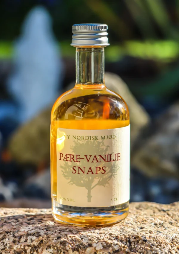 Flaske med Pære-Vanilje Snaps på 5 cl med gylden væske, placeret på en sten udendørs.