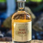 Flaske med ribssnaps, 5 cl, med klar gylden væske og label med teksten 'Ribs Snaps'.