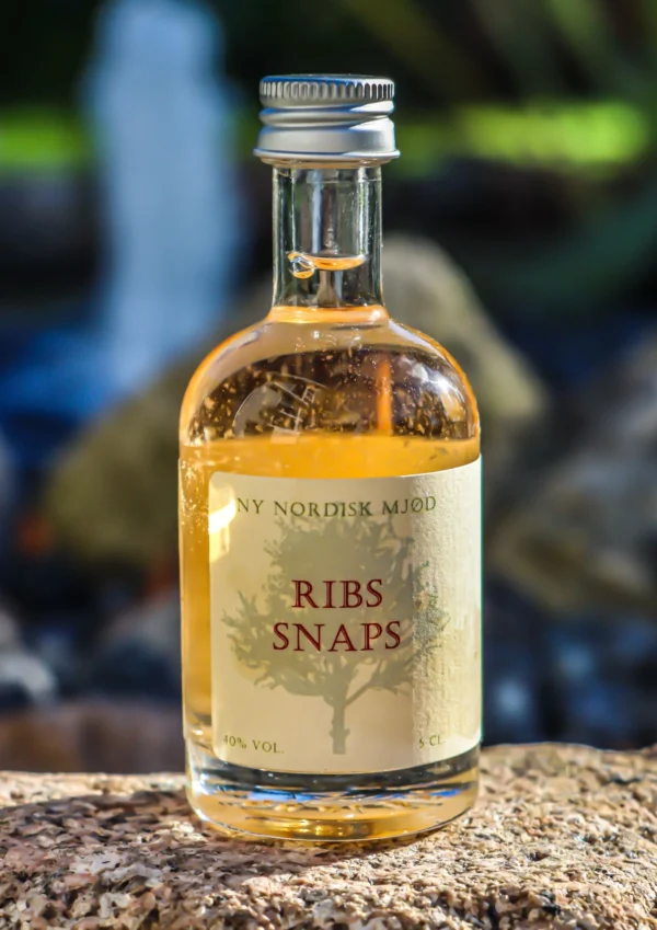 Flaske med ribssnaps, 5 cl, med klar gylden væske og label med teksten 'Ribs Snaps'.