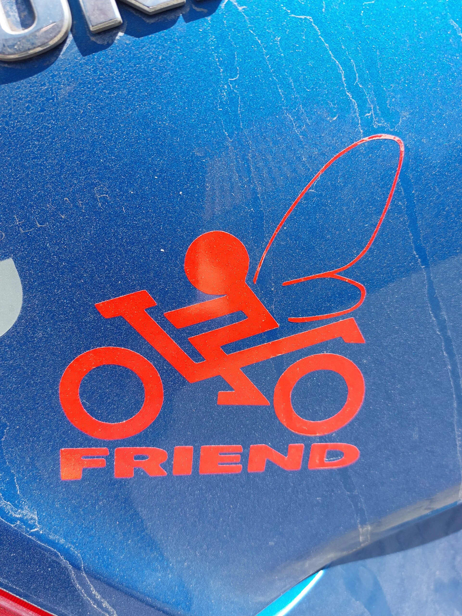 Nærbillede af et rødt Bikerfriend Skyts Fe klistermærke på et støvet, midnatsblåt underlag med struktureret overflade.