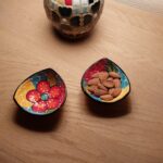 Nærbillede af to farverige, håndmalede tapasskåle, den ene med mandler, med en mosaiklampe i baggrunden.