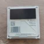 Bagsiden af et gennemsigtigt navneskilt med en sort magnetstribe og en stregkode samt instruktioner.