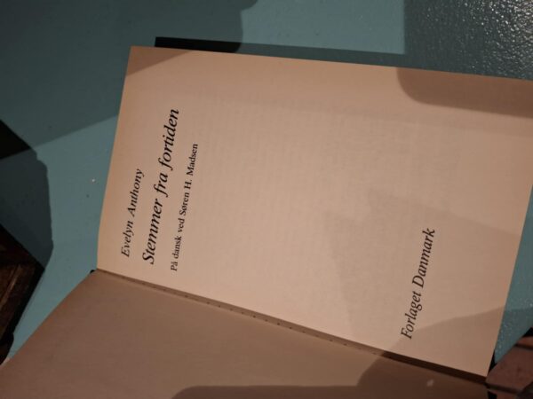 Indersiden af bogen 'Stemmer fra fortiden' af Evelyn Anthony, der viser titel, forfatter og forlag 'Forlaget Danmark'.
