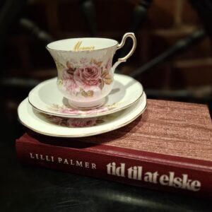 Bogen 'Tid til at elske' af Lilli Palmer ligger under et elegant hvidt tesæt med lyserøde roser og guldkant.