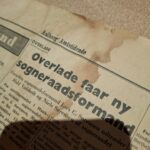 Detalje af gammelt avispapir 'Aalborg Amtstidende' i bunden af en åben mørkegrøn Vulkolit rejsekuffert, der beskytter indholdet.