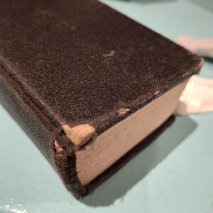 En Den Danske Salmebog i slidt, sort læderindbinding, der ses tæt på. Bogen ligger på en lyseblå overflade.