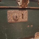Et nærbillede af en rusten lås på en mørkegrøn vintage rejsekuffert.