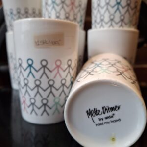 En række hvide porcelænskopper fra Mette Ditmer by Aida med farvede, sammenholdte figurer. Billedet viser også et '12 stk. kr. 400,-' prismærke.