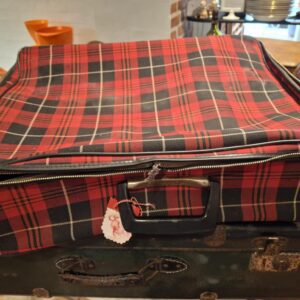 En rødrutet vintage kuffert med sort og beige, placeret oven på en mørkegrøn kuffert, med et lille hjertevedhæng.