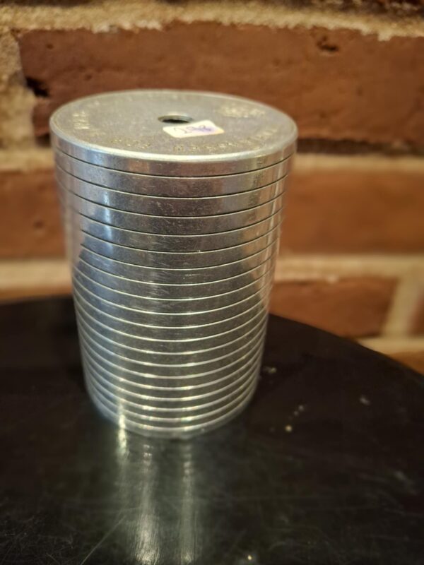 En cylindrisk sparebøsse i metal med stabelbare ringe og indgraveret tekst, står på sort overflade.