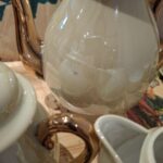 Nærbillede af en vintage tekande med perlemorsfinish og gulddetaljer, der reflekterer de andre dele af tesættet.