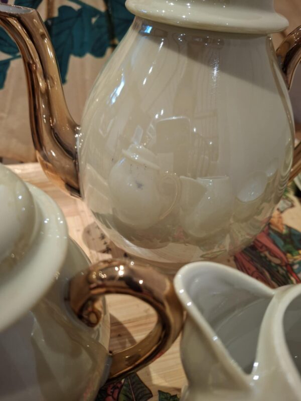 Nærbillede af en vintage tekande med perlemorsfinish og gulddetaljer, der reflekterer de andre dele af tesættet.