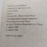 Den skindøde u-båd af Len Deighton. Blå og hvidt cover med en mand med en kniv og sort uniform.