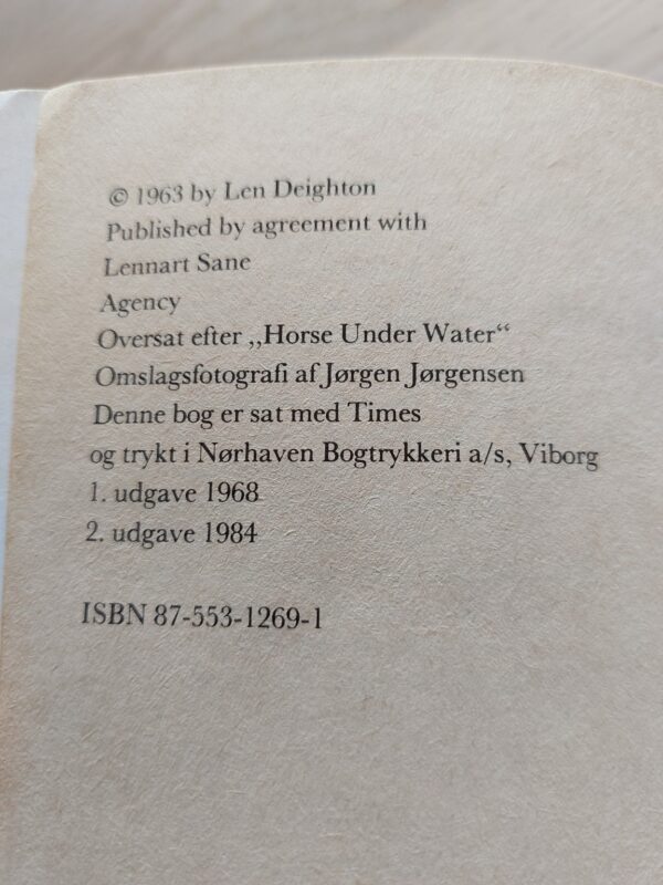 Den skindøde u-båd af Len Deighton. Blå og hvidt cover med en mand med en kniv og sort uniform.