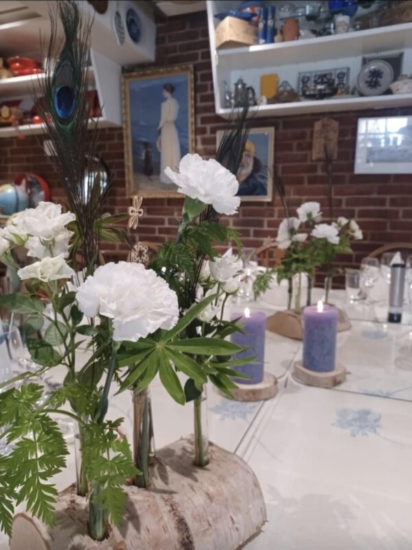 En blomsterholder af barkbeklædt træstykke med fire tomme glasrør. Vedbendplanter er arrangeret rundt om den på en dug.