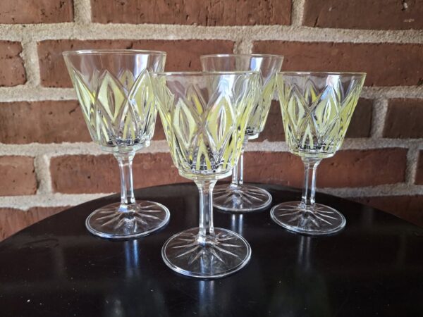 Fire klare aperitifglas med grønt rombeformet mønster, stående på en mørk overflade foran en murstensvæg.