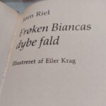 Nærbillede af bogryggen på 'Frøken Biancas dybe fald' af Jørn Riel, med grønt og beige design og gulddetaljer.