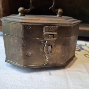 En klar souvenirflaske med motiv af Krudttårnet Frederickshavn og et rustikt messing-skrin med patina, placeret på en træhylde.