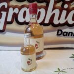 Et stort butiksskilt fra 'Chocolate Graphics Danmark' i beige og brunt, placeret bag to flasker julemjød og en krystalskål med chokolade på en hvid dug.