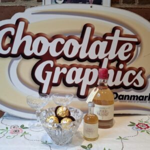 To flasker Julemjød fra Ny Nordisk Mjød, en stor og en lille, stående foran et 'Chocolate Graphics Danmark' skilt på en hvid dug.