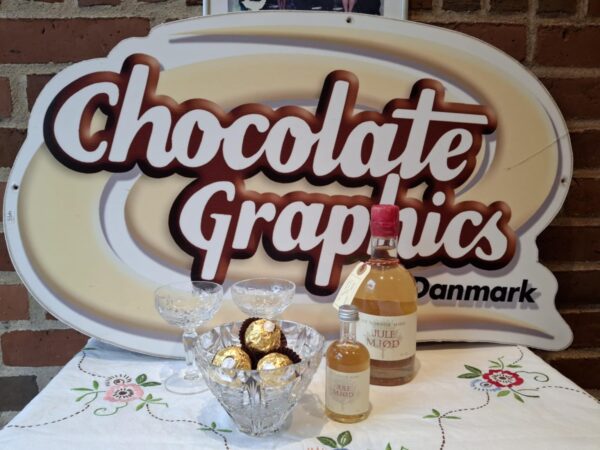 To flasker Julemjød fra Ny Nordisk Mjød, en stor og en lille, stående foran et 'Chocolate Graphics Danmark' skilt på en hvid dug.