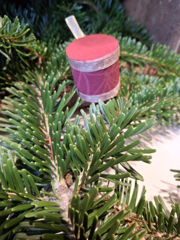 Et lille, håndlavet juletrommeophæng med et mønster af blå blomster og et matchende blåt satinbånd. Ophængt i juletræets grangrene.