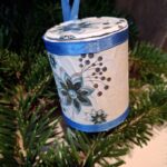 Et lille, håndlavet, rødt juletrummeophæng dekoreret med hvidt/sølvbånd med kristtjørneblade og hvide snore. Hænger i juletræets grangrene.