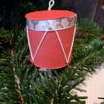 Et lille, håndlavet juletromme ophæng i rød og grøn med julemotiver af kristtjørn. Hænger i juletræets grangrene.