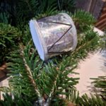 Et lille, håndlavet juletromme ophæng i rød og grøn med hvid kristtjørn mønster og rødt bånd. Hænger i juletræets grangrene.