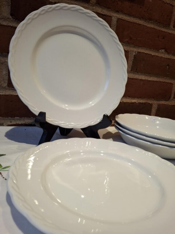 En stak hvide, flade Hanley Ware 'Satin White' tallerkener med elegant reliefkant, en står oprejst, foran murstensvæg.
