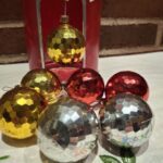 En samling vintage julekugler i rød, gul og sølv, alle med et sekskantet reliefmønster, foran en rød metaldåse.
