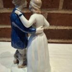 Bagsidebillede af en Schwarzburger porcelænsfigur af et dansende par. Manden i blå jakke, kvinden i hvid kjole, tæt sammen.
