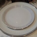 En Rosenthal Capri tallerken med et delikat gråt og pink mønster og en elegant guldkant, delvist skjult af andre tallerkener.