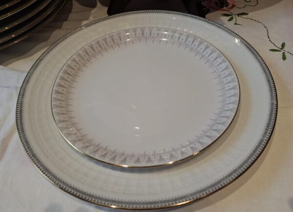 En Rosenthal Capri tallerken med et delikat gråt og pink mønster og en elegant guldkant, delvist skjult af andre tallerkener.