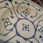 En Kahla Fattigmands muselmalet tallerken i hvid porcelæn med blåt mønster, set lidt fra oven med et fokus på dekorationerne.
