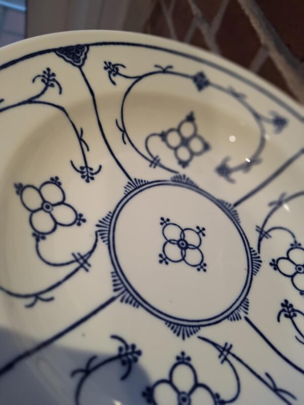 En Kahla Fattigmands muselmalet tallerken i hvid porcelæn med blåt mønster, set lidt fra oven med et fokus på dekorationerne.