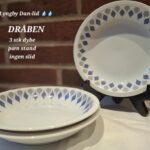 Tre dybe, hvide Lyngby Danild 'Dråben' tallerkener med blåt og gråt dråbemønster. To er stablet, en står oprejst.