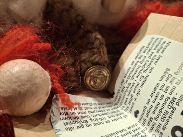 Nærbillede af en nisses overkrop. Man ser flettede detaljer, skæg af vat og en gammel guldfarvet knap.