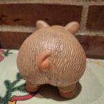 Bagsiden af en terracotta sparegris, der viser dens krøllede hale og teksturerede overflade. På juledug.