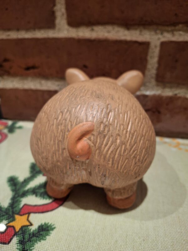 Bagsiden af en terracotta sparegris, der viser dens krøllede hale og teksturerede overflade. På juledug.