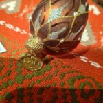 Et aflangt, hånddekoreret juleornament i kobber- og guldnuancer med glimmerede detaljer og diamanter.