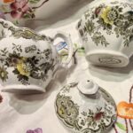 En nærbillede af en engelsk porcelænsflødekande i hvid med blomster- og fuglemotiv, med synlig krakelering på overfladen.