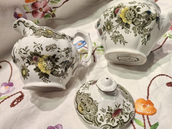 En nærbillede af en engelsk porcelænsflødekande i hvid med blomster- og fuglemotiv, med synlig krakelering på overfladen.