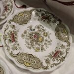 En Ridgway 'Windsor' underkop eller sidetallerken i hvid porcelæn med grønne og brune blomstermotiver og en bølget kant.