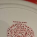 Nærbillede af bagsiden af en Woodland tallerken fra Wood & Sons med rødt stempel, der indikerer 'WOODLAND' og producentinformation.