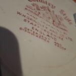 Nærbillede af bagsiden af en W.H. Grindley 'Country Style' tallerken med rødt bundstempel og information om producenten.
