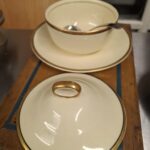 Komplet sart creme marmeladekrukkesæt fra Victorian Johnson Bros. bestående af krukke, låg med guldkant og en underskål, pyntet med guldkant og mørkeblå detaljer. En lille ske er også synlig.