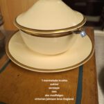 Sart creme marmeladekrukke med låg og tilhørende underskål fra Victorian Johnson Bros., dekoreret med guldkant. Set fra siden med hvid tekst: '1 marmelade krukke sukker senneps mm. ske medfølger. virtorian johnson bros England'.