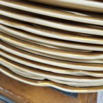 Stabel af antikke middagstallerkener i cremefarvet porcelæn med guldkant, set fra siden, der tydeligt viser guldkantens oxidation og den gyldne patina.